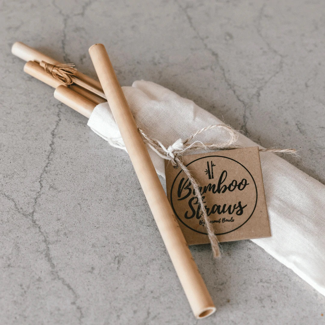 Set of four bamboo straws with organic cotton pouch on a textured surface.